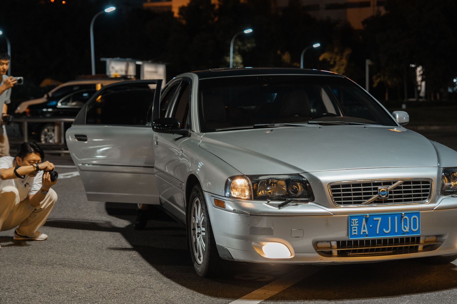 Chauffeur holding the rear door of a black car at night