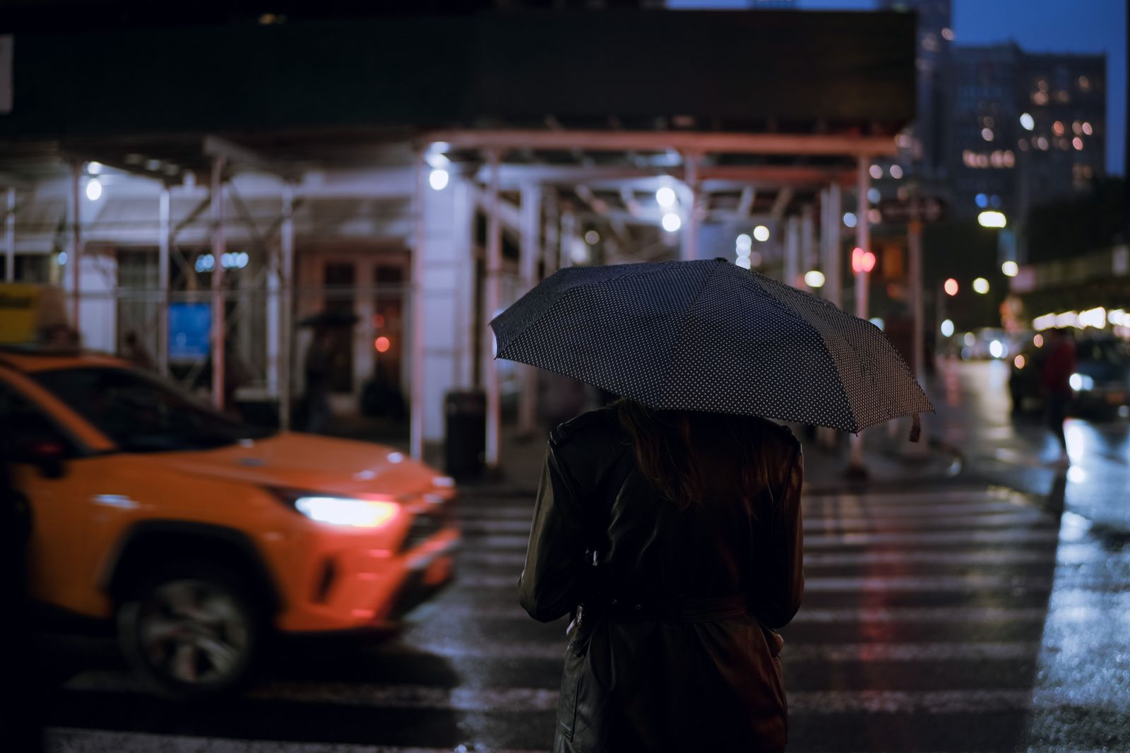 A black sedan waiting on a wet city street at night