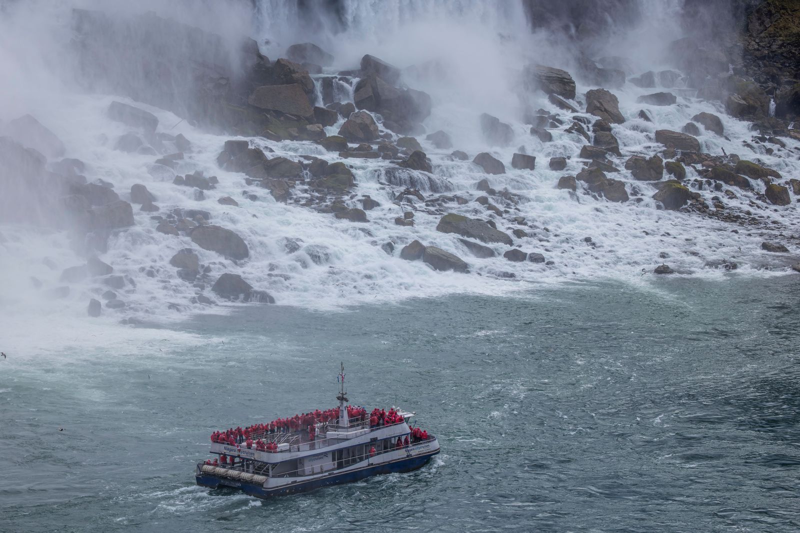 Visitors in ponchos on a boat tour heading into the mist of the falls