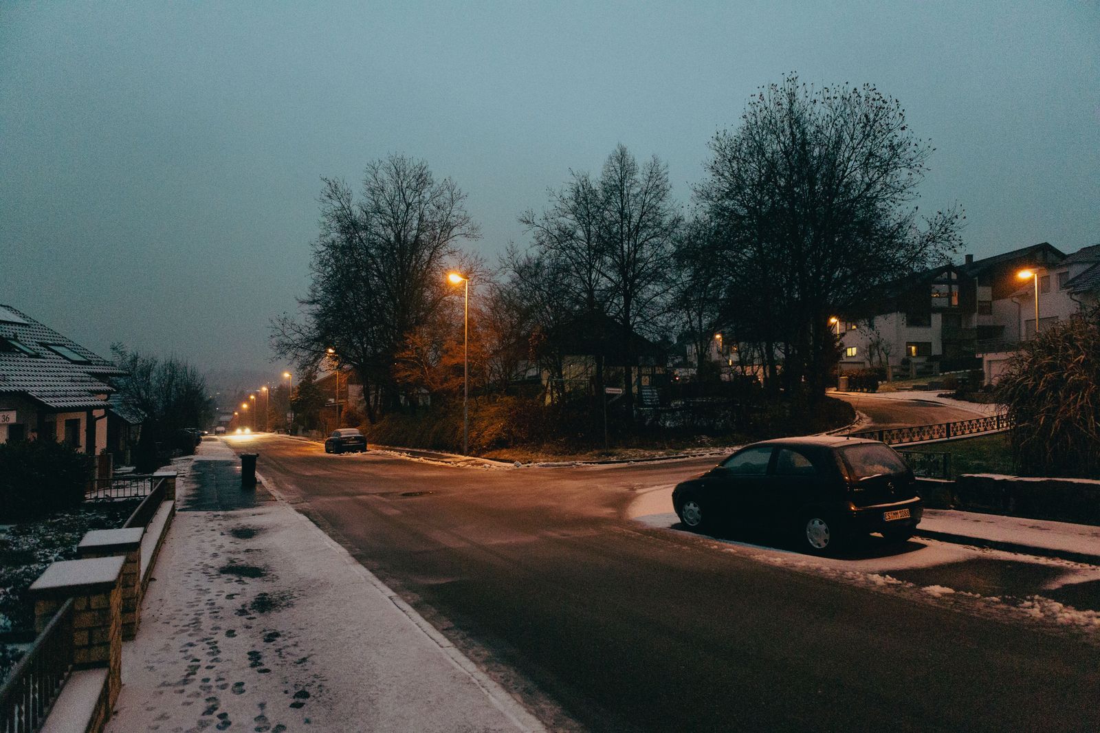 A quiet suburban street before dawn with a car waiting at the curb