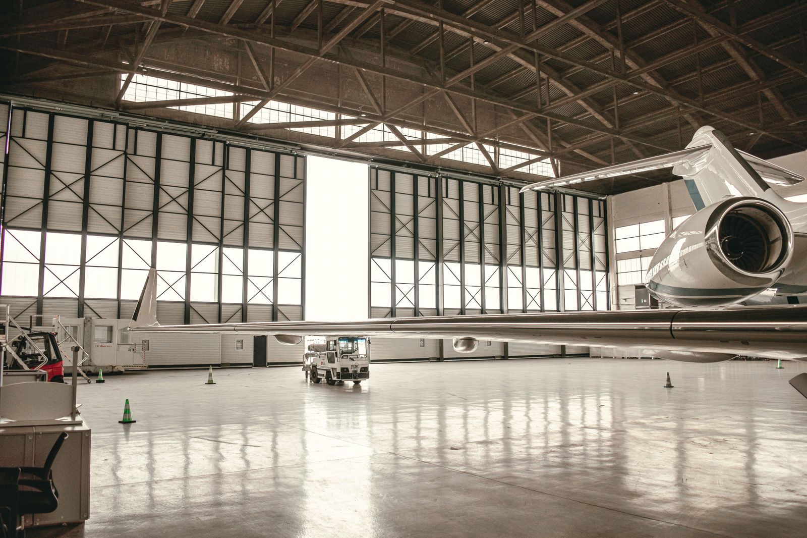 A chauffeur holding the rear door of a black sedan for a passenger outside a hangar