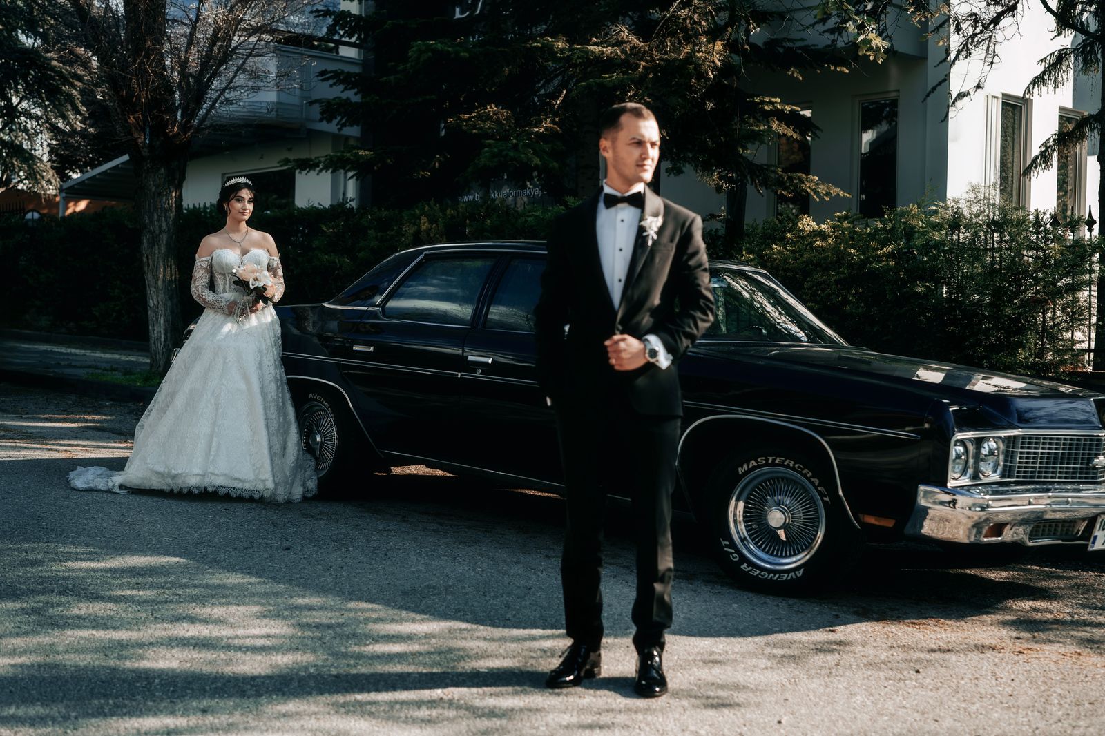 A wedding couple beside a classic luxury car on their wedding day
